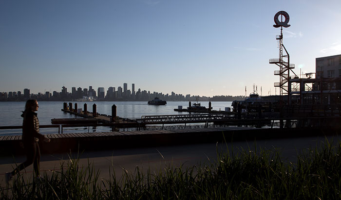 A woman walking by a grassy field in the background is the Lonsdale quay Q