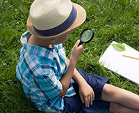 A kid, wearing a fidora, looking through a magnifying glass